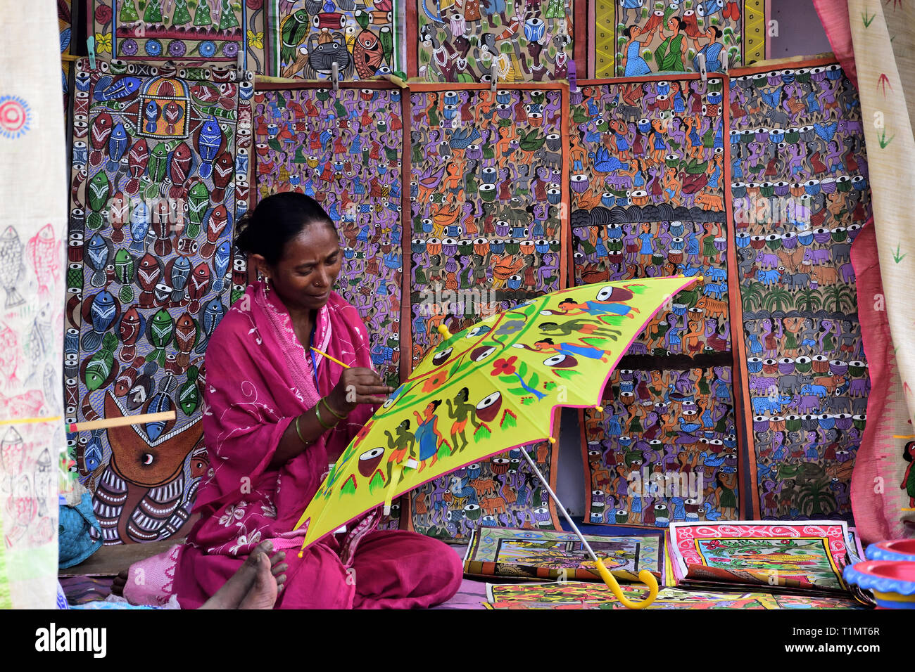 Femme artiste rurales indiennes est la peinture d'un parapluie assis par mur avec décorations suspendues Banque D'Images