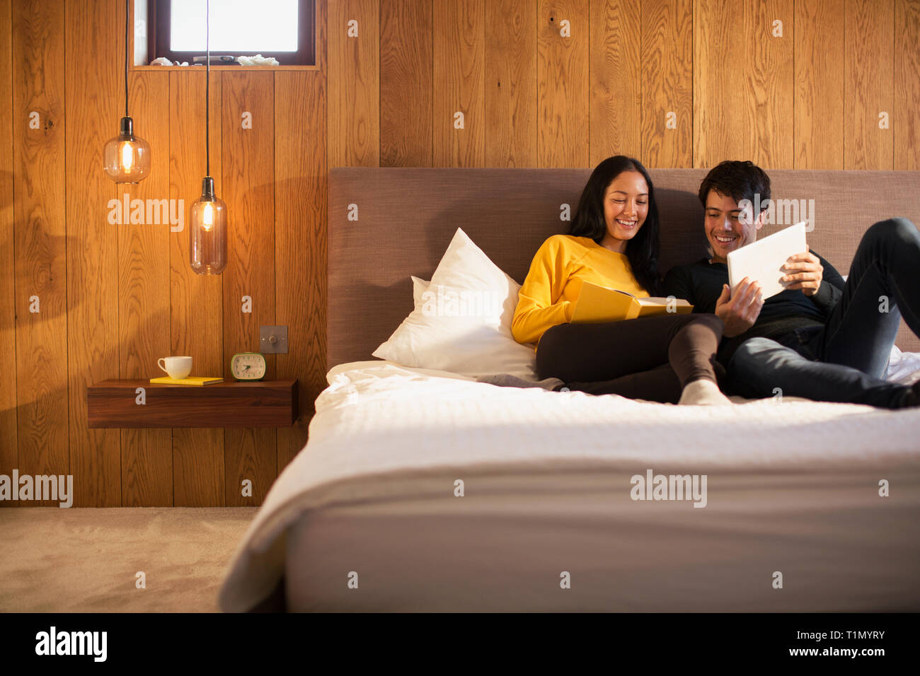 Couple reading book et using digital tablet in bed Banque D'Images