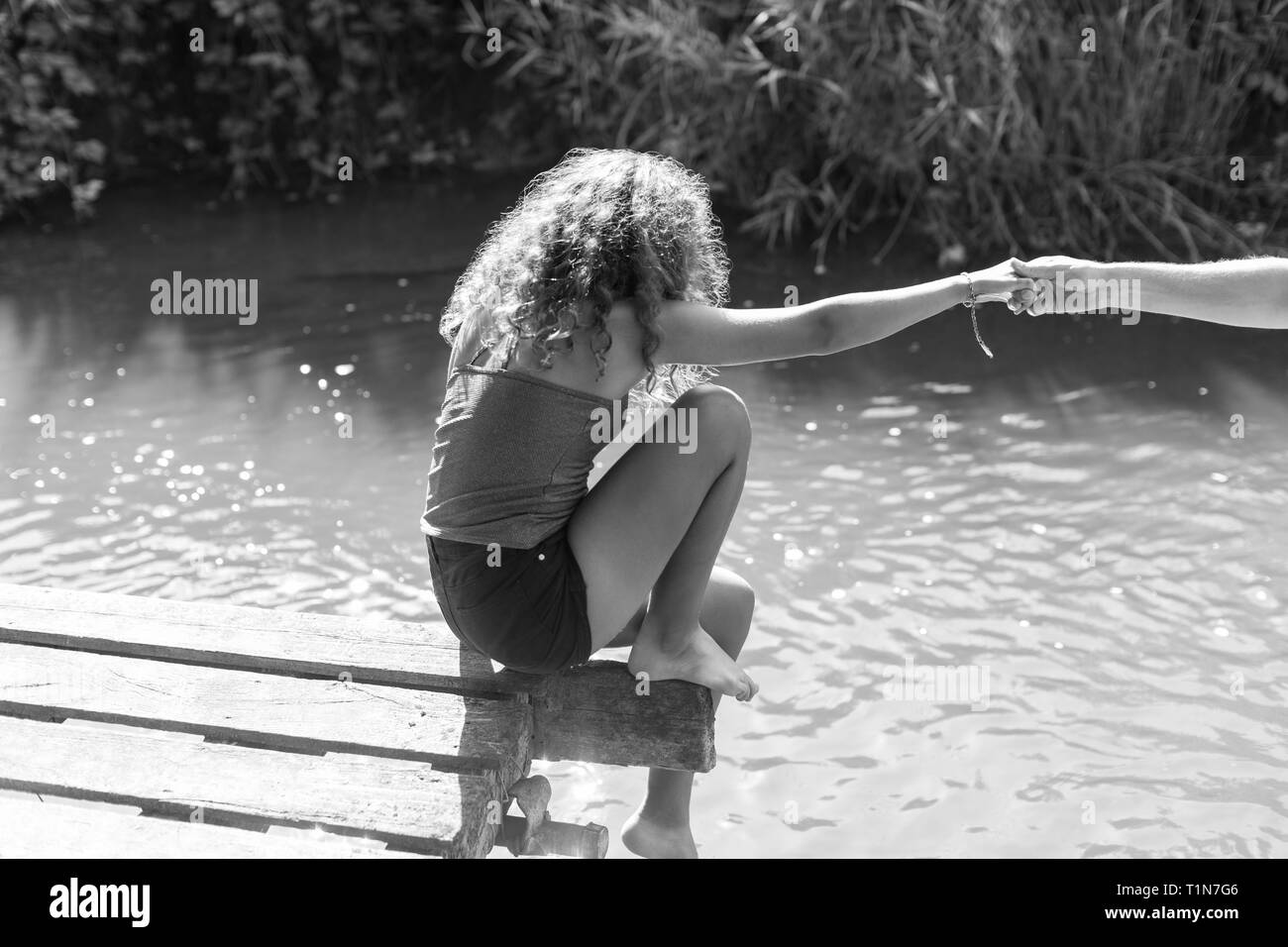 Fille assise au bord du quai de la rivière ensoleillée Banque D'Images