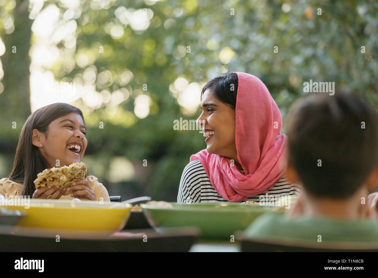 Mère et fille en hijab rire at dinner table Banque D'Images