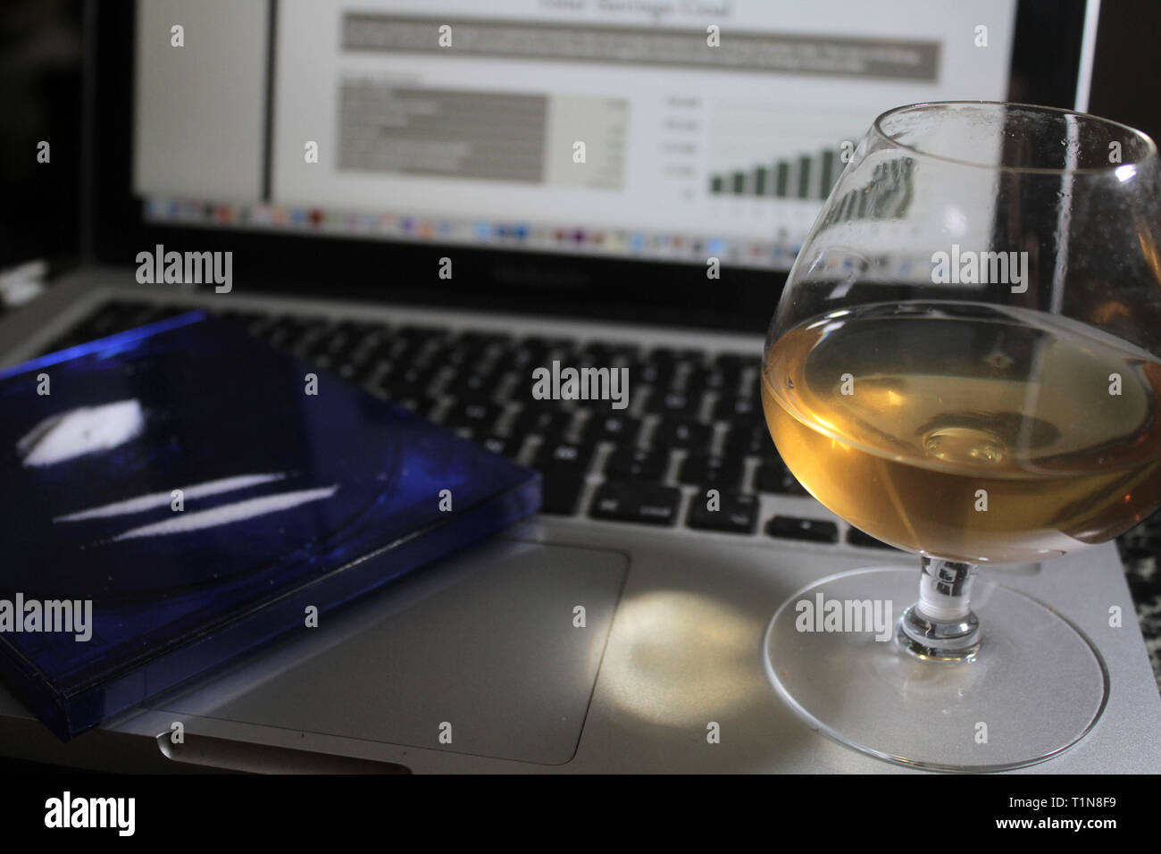 Ordinateur portable avec de l'alcool dans le verre et soft focus la cocaïne et vers le haut sur l'écran graphique en arrière-plan d'alcool et de la cocaïne de travail à distance en ligne Banque D'Images