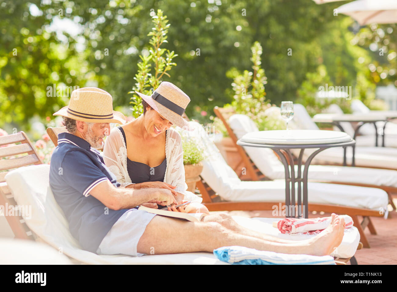 Couple, livre et lecture à l'aide de smart phone on lounge chair at poolside resort Banque D'Images