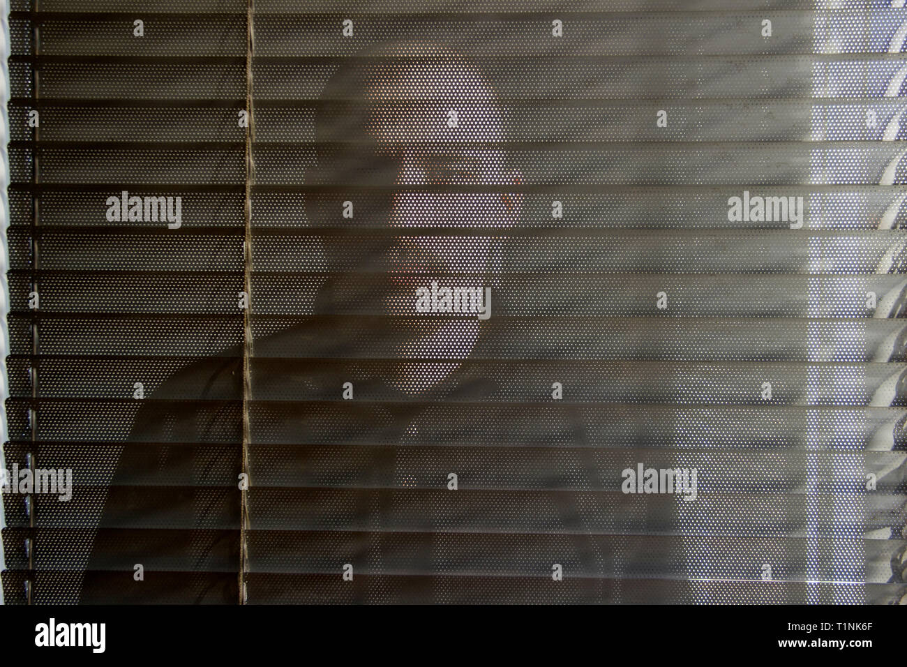 Homme avec une moustache debout derrière la porte en verre avec stores pare-soleil Banque D'Images