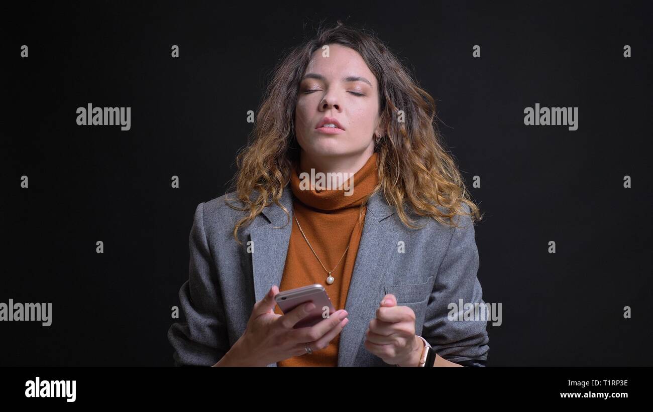 De jeunes pousses Gros plan femme caucasienne attrayant des messages sur le téléphone et être irrité devant la caméra avec isolé sur fond noir Banque D'Images