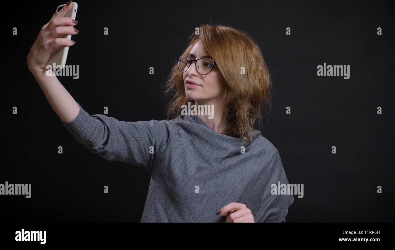 Closeup portrait of middle-aged femme rousse extravagante dans les verres en tenant vos autoportraits sur le téléphone en face de l'appareil photo Banque D'Images