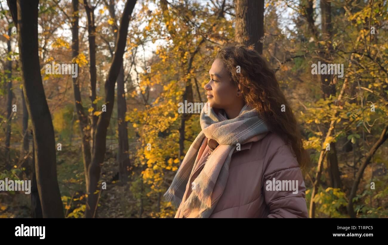 Portrait de profil de smiling curly-haired woman walking in autumnal park et en observant la beauté. Banque D'Images
