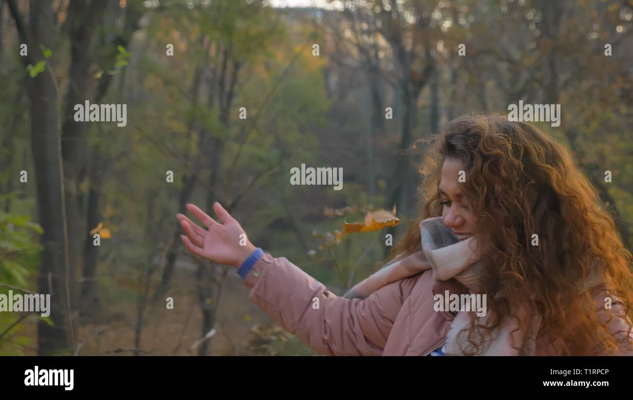 Portrait of smiling curly-haired woman throwing quitte joyeusement dans le parc d'automne. Banque D'Images