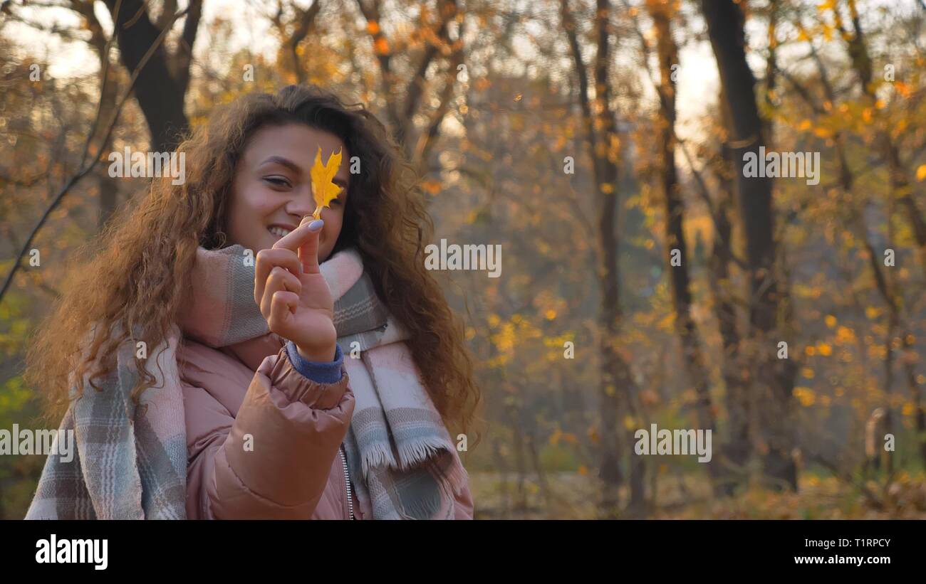 Portrait of smiling caucasian girl aux cheveux bouclés feuille jaune en montrant la joie d'automne, l'appareil photo. Banque D'Images