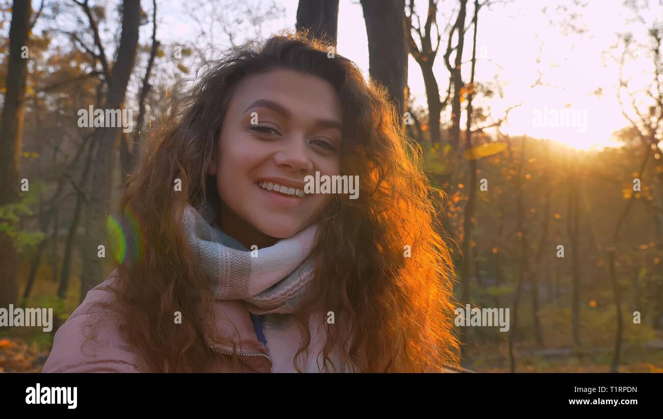 Les selfies photo de jeune fille de race blanche aux cheveux bouclés en souriant en regardant dans l'appareil photo d'automne ensoleillée park. Banque D'Images
