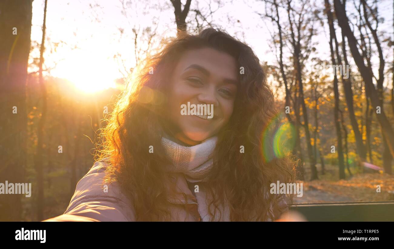 Les selfies photo de Mignon aux cheveux bouclés caucasian girl heureusement en appareil photo dans le parc d'automne ensoleillé. Banque D'Images