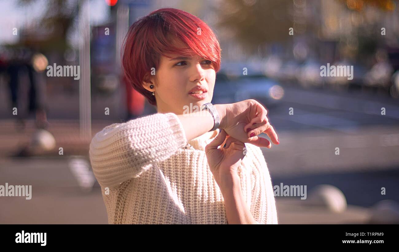 Portrait de jeune fille aux cheveux roses caucasienne de parler à l'aide de ses montres sur fond de la ville ensoleillée. Banque D'Images
