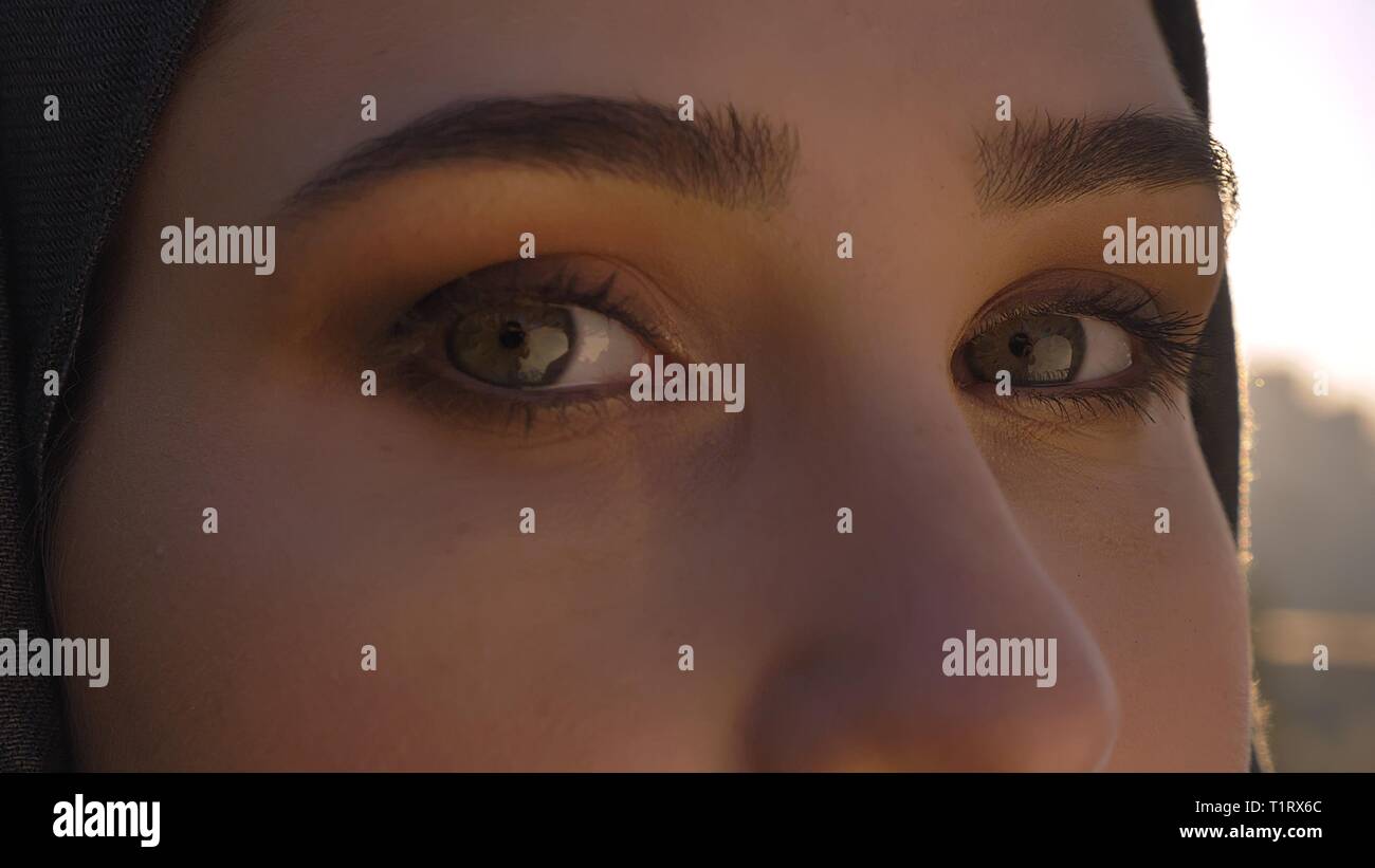 De jeunes pousses Gros plan jolie visage de femme en hijab avec les yeux regardant droit à l'appareil photo avec urban city sur l'arrière-plan Banque D'Images