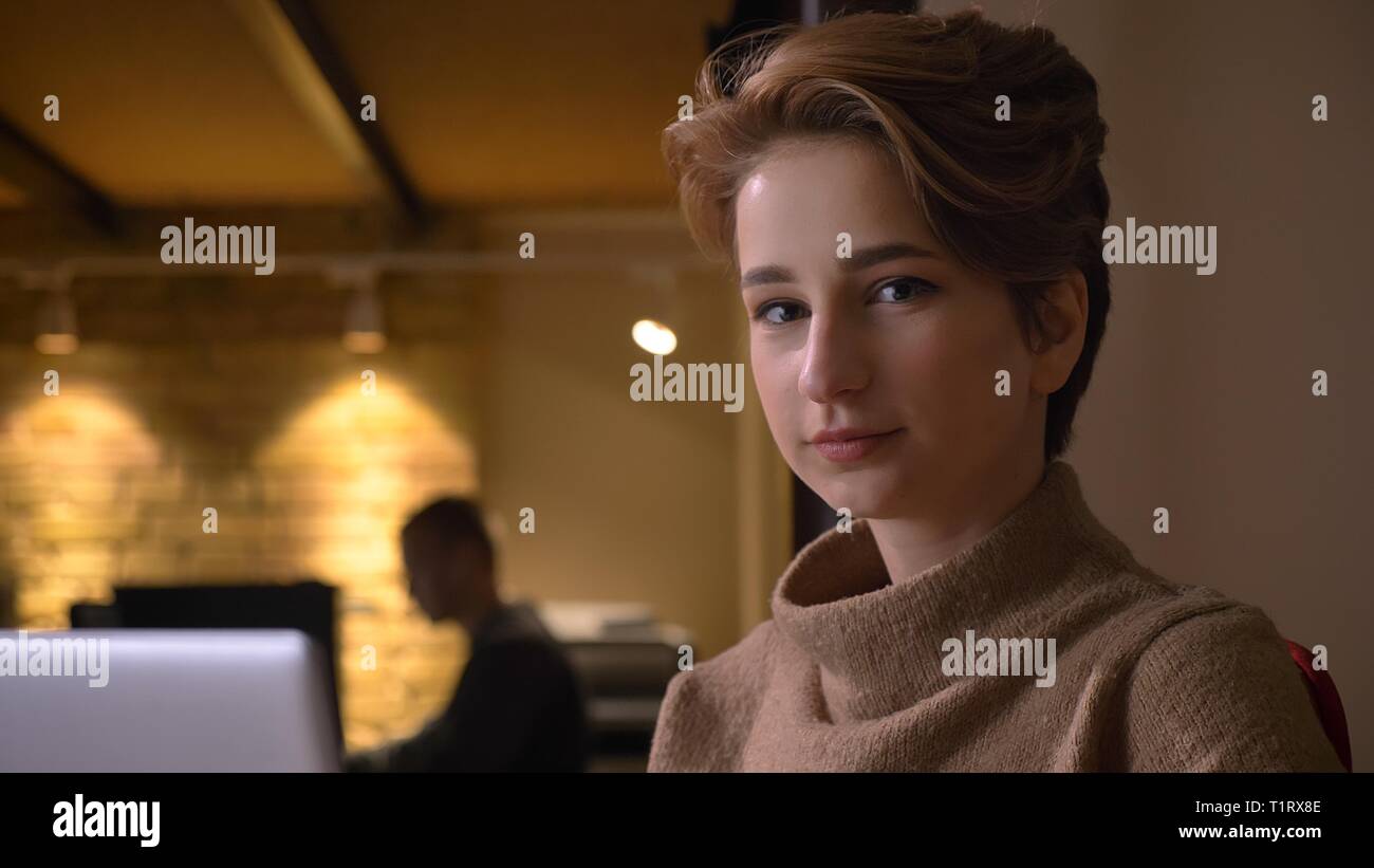 De jeunes pousses Gros plan belle caucasian businesswoman en utilisant l'ordinateur portable à la caméra et à l'intérieur dans le bureau en souriant Banque D'Images