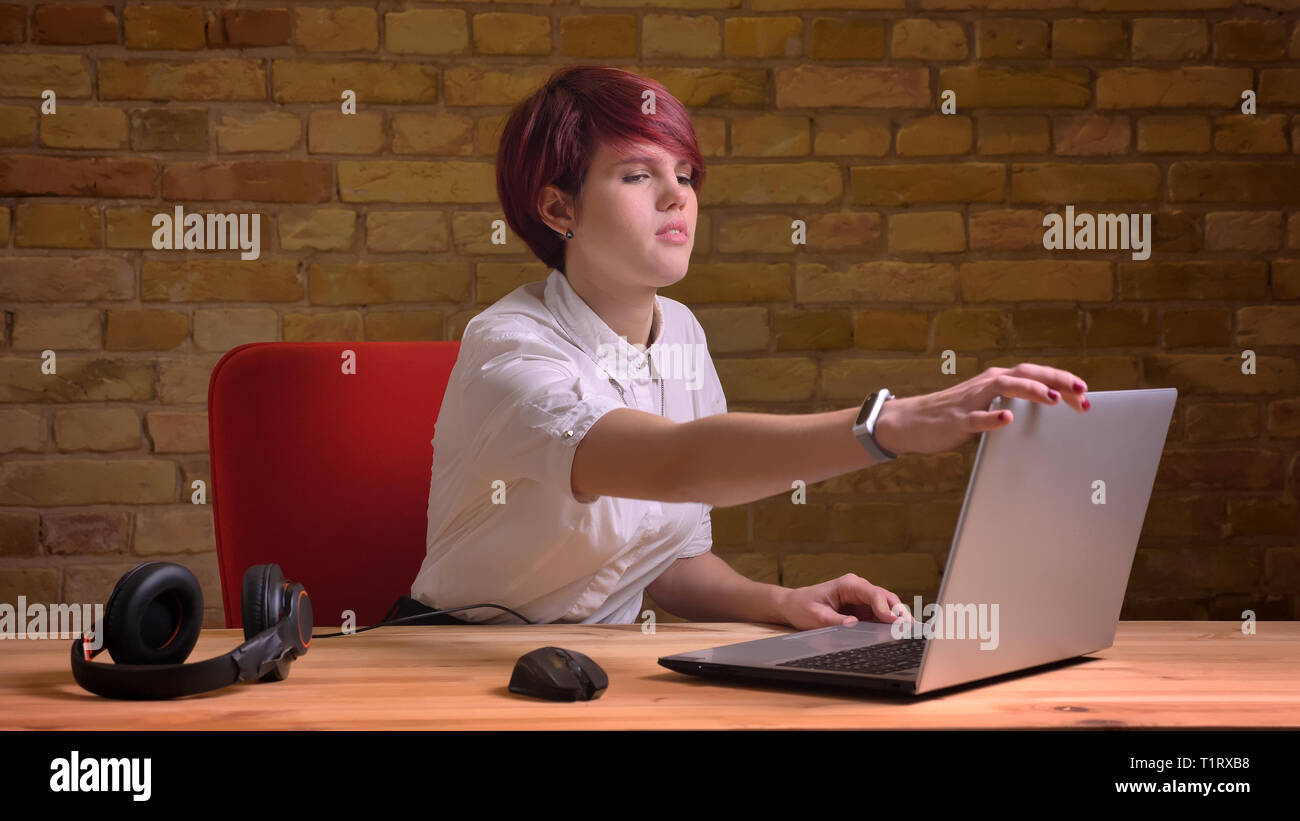 De jeunes pousses Gros plan jolie femelle vidéo hipster blogger avec les cheveux teints fixant l'ordinateur portable et le streaming live avec un casque sur la table Banque D'Images