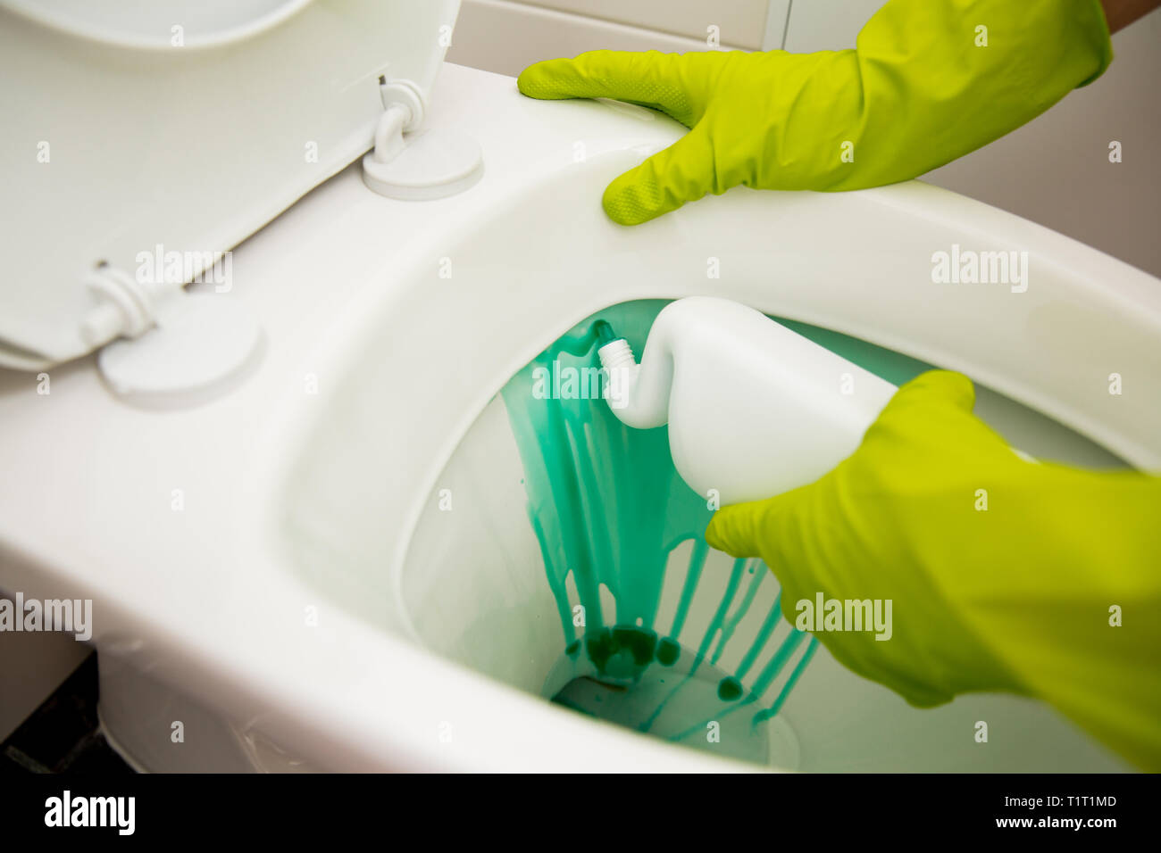 Dans l'homme gants de protection en caoutchouc, nettoyage lave-toilettes avec brosse et une bouteille de l'agent de nettoyage dans les mains. Détergent liquide vert dégoulinant de toilettes Banque D'Images