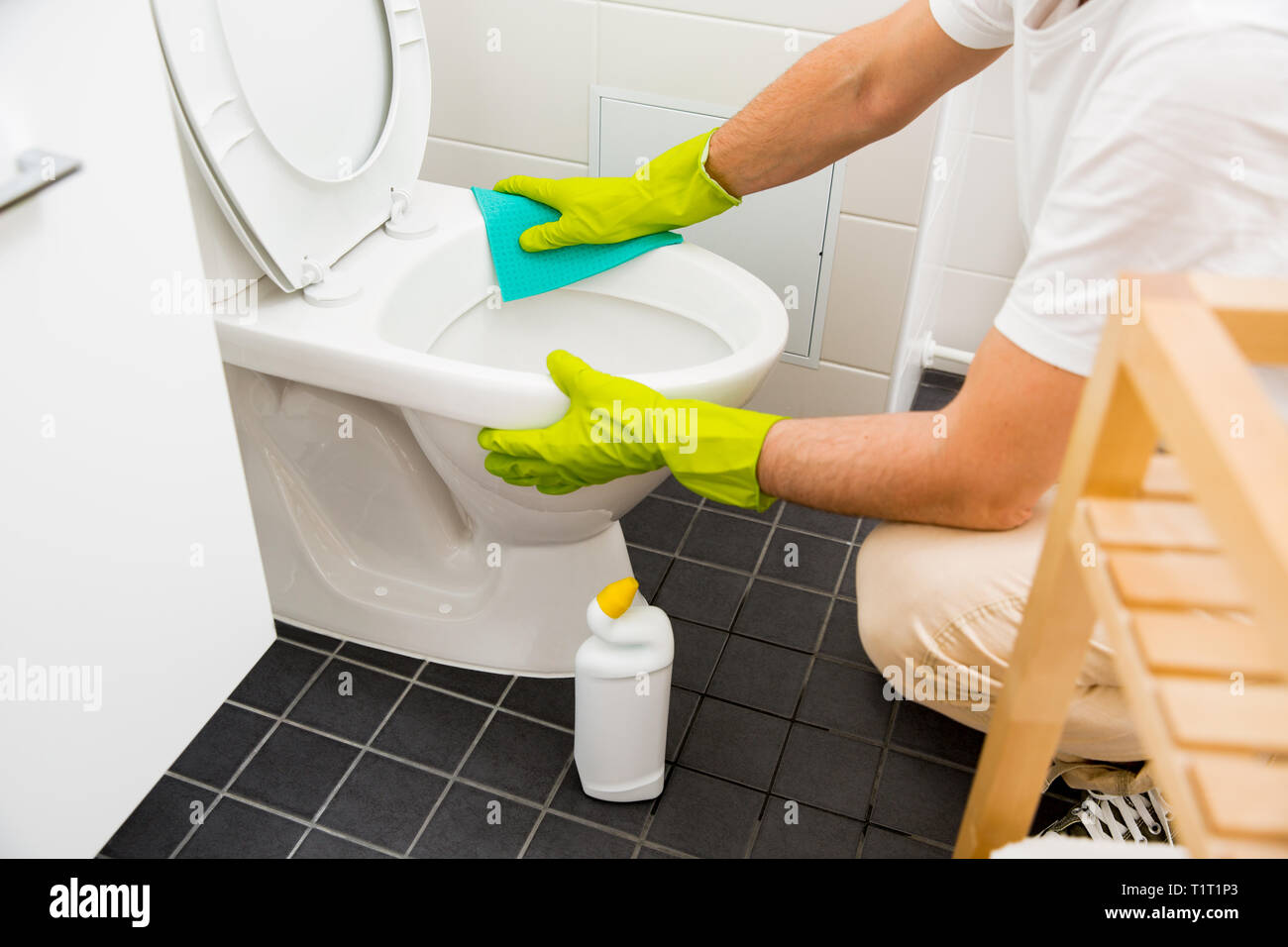Dans l'homme gants de protection en caoutchouc, nettoyage lave-toilettes avec brosse et une bouteille de l'agent de nettoyage dans les mains. Détergent liquide vert dégoulinant de toilettes Banque D'Images
