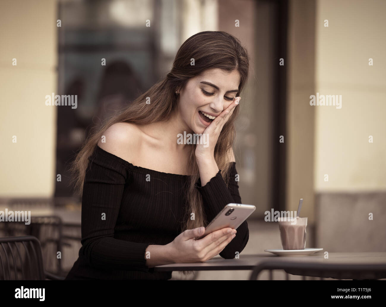 Jolie jeune femme élégante heureux de boire du café, de la consultation des messages et aime sur smart mobile phone au café terrasse. Dans le mode de vie, blogger et Banque D'Images