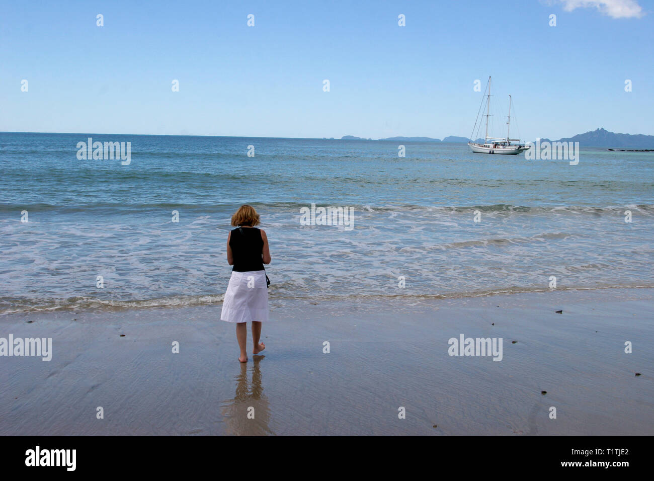 NEW ZEALAND woman at beach à la recherche à l'horizon et sailingboat pour anchor Banque D'Images