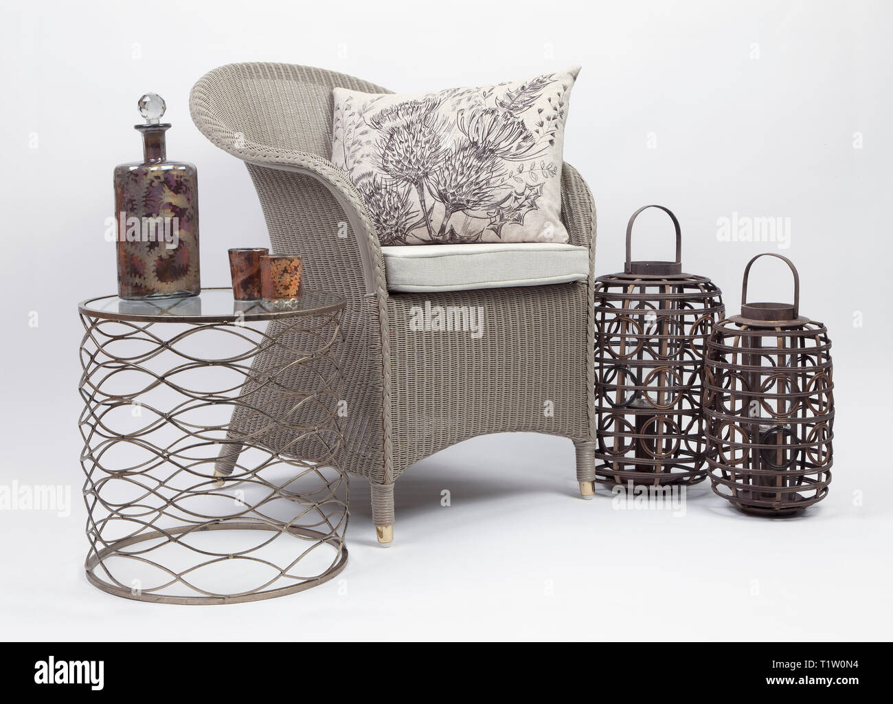 Wicker Chair et coussins avec une petite table et deux porte-bougie en osier sur un fond blanc Banque D'Images