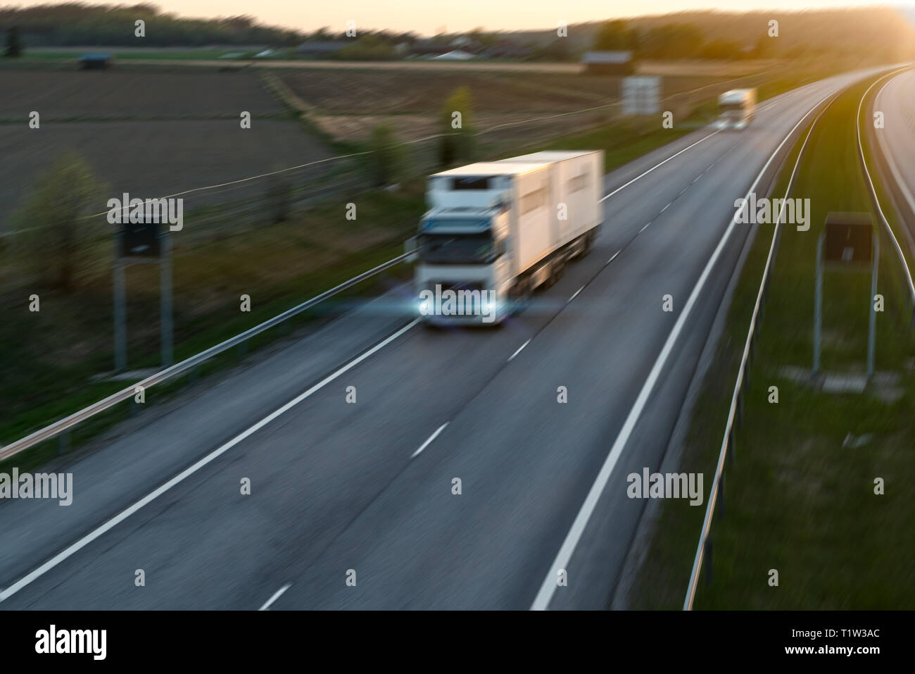 Deux camions de fret roulant sur l'autoroute au coucher du soleil avec effet de flou. Banque D'Images