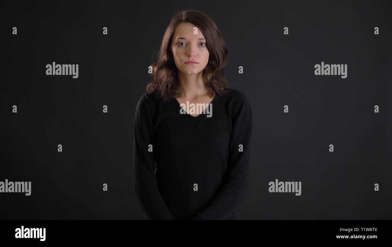 Portrait de jeune femme brune fragile regardant tristement et pensivement en huis clos sur fond noir. Banque D'Images