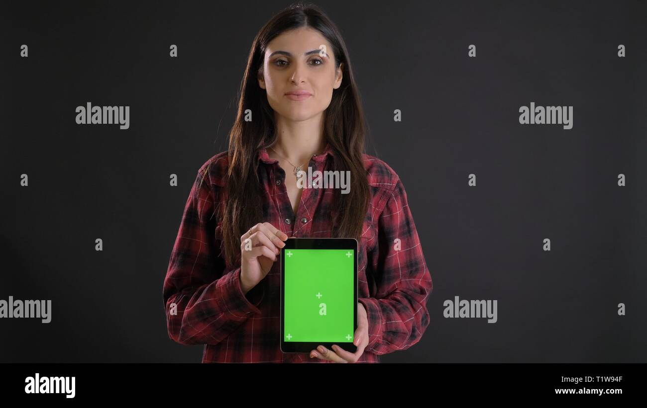 Portrait de jeune fille aux cheveux long en plaided shirt démontrant à la verticale de l'écran vert comprimé sur fond noir. Banque D'Images