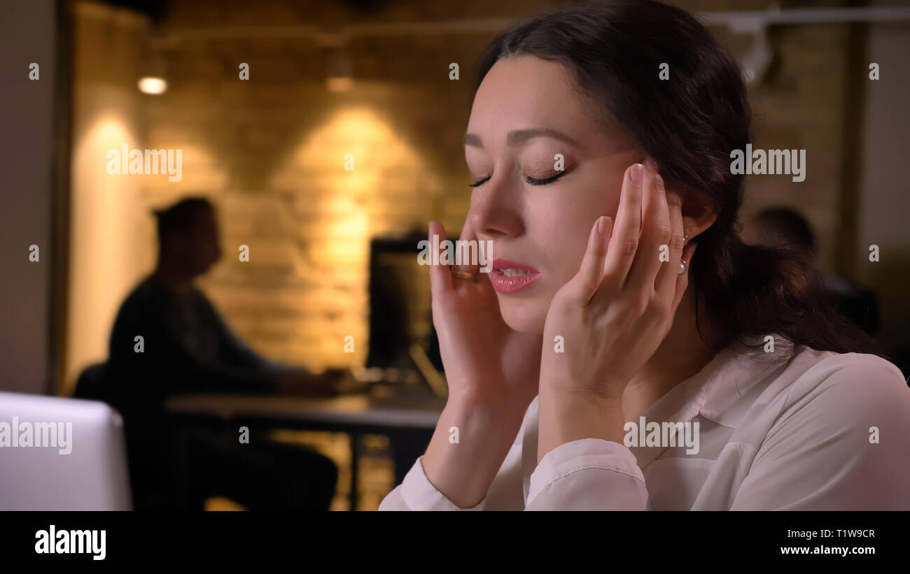 De jeunes pousses Gros plan jolie femme employée ayant un mal de tête tout en tapant sur l'ordinateur portable à l'intérieur sur le lieu de travail Banque D'Images