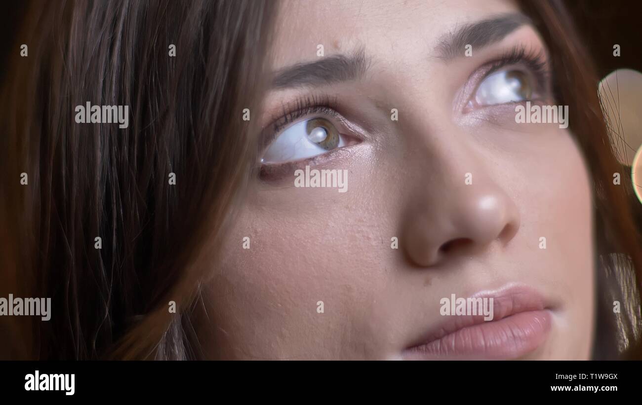Close-up eye-portrait de belle caucasian brunette girl rêveusement vers le haut sur l'arrière-plan Lumières floues. Banque D'Images