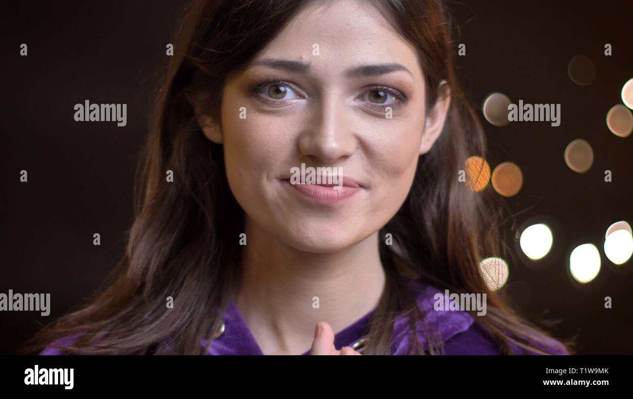 Close-up portrait of gorgeous young brunette girl avec calme sourire dans le fond de l'appareil photo Lumières floues. Banque D'Images