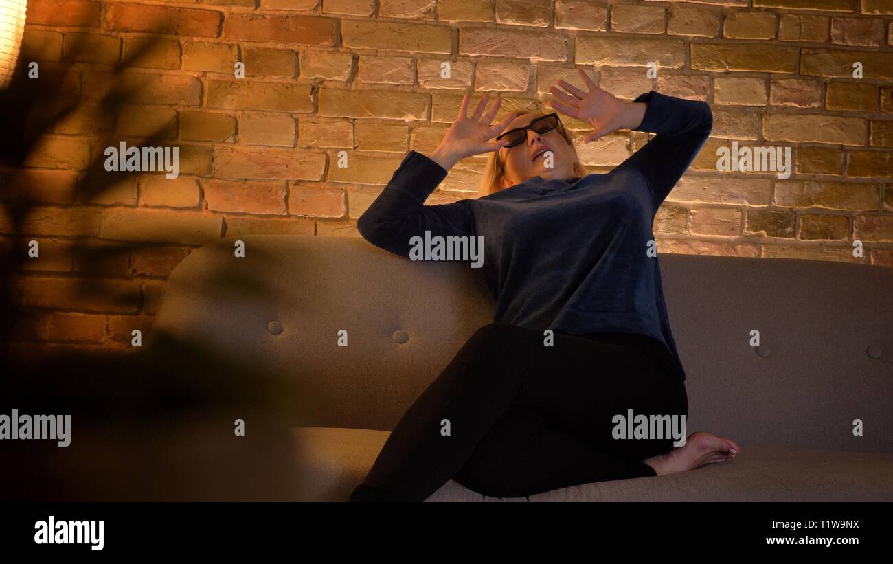 Extrêmement peur portrait dame de lunettes 3D à regarder un film d'horreur et de masquer par ses mains dans une atmosphère familiale. Banque D'Images