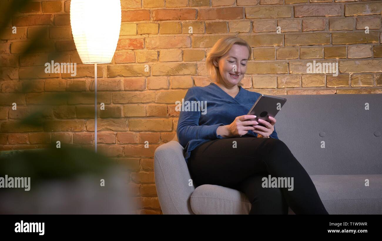 Portrait of senior woman femme assise sur un canapé et regarder dans tablet volontiers dans une atmosphère cosy home. Banque D'Images