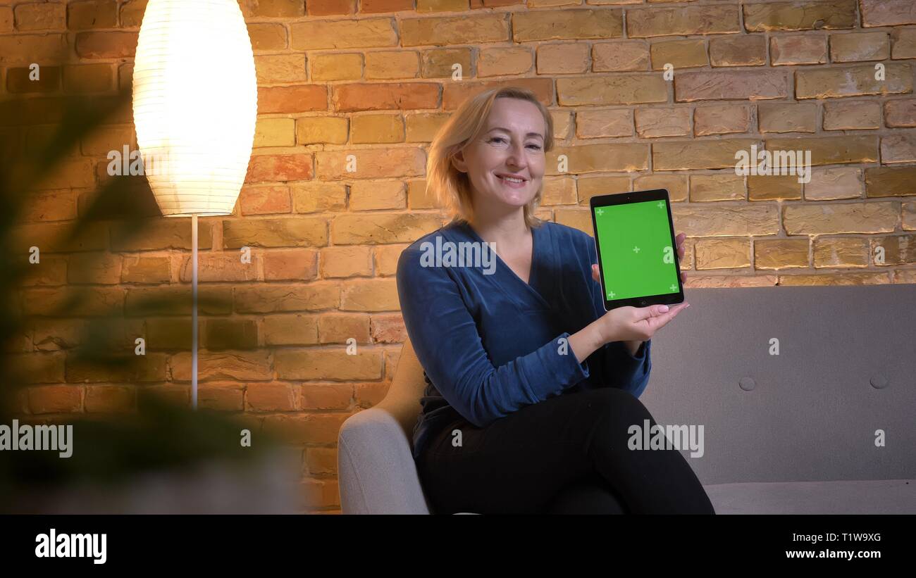 Portrait of young lady montrant l'écran vert de tablette en huis clos dans une atmosphère familiale. Banque D'Images