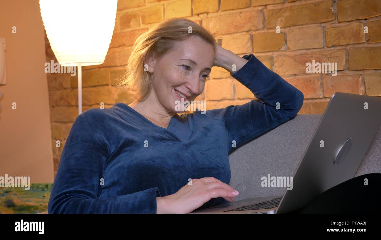 Portrait of senior woman femme assise sur un canapé et le travail avec ordinateur portable en souriant en maison chaleureuse atmosphère. Banque D'Images