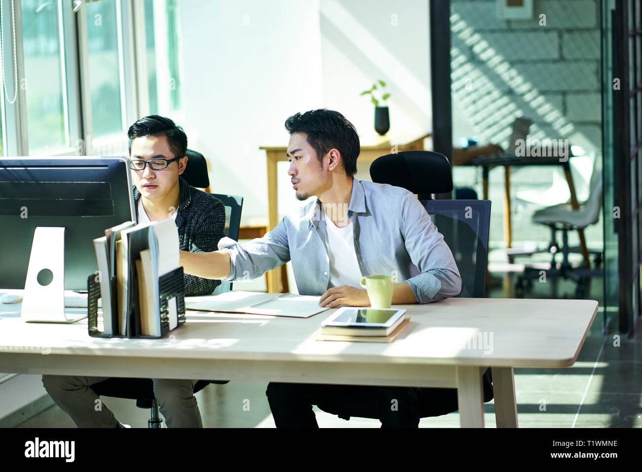 Deux jeunes gens d'affaires asiatiques travaillant ensemble en fonction de discuter affaires avec ordinateur de bureau. Banque D'Images