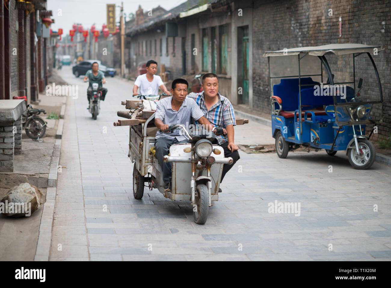 Pingyao, Chine - 0814 2016 : deux adultes sur un tricycle transportant des pièces de bois. Deux travailleurs sur un vélo à trois roues dans une rue de Pingyao, Shan Banque D'Images