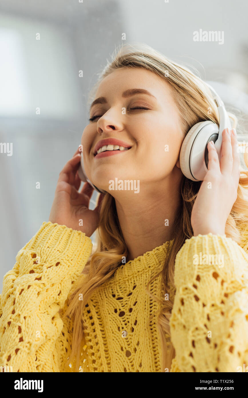 Selective focus of beautiful smiling young woman in headphones listening music at home Banque D'Images