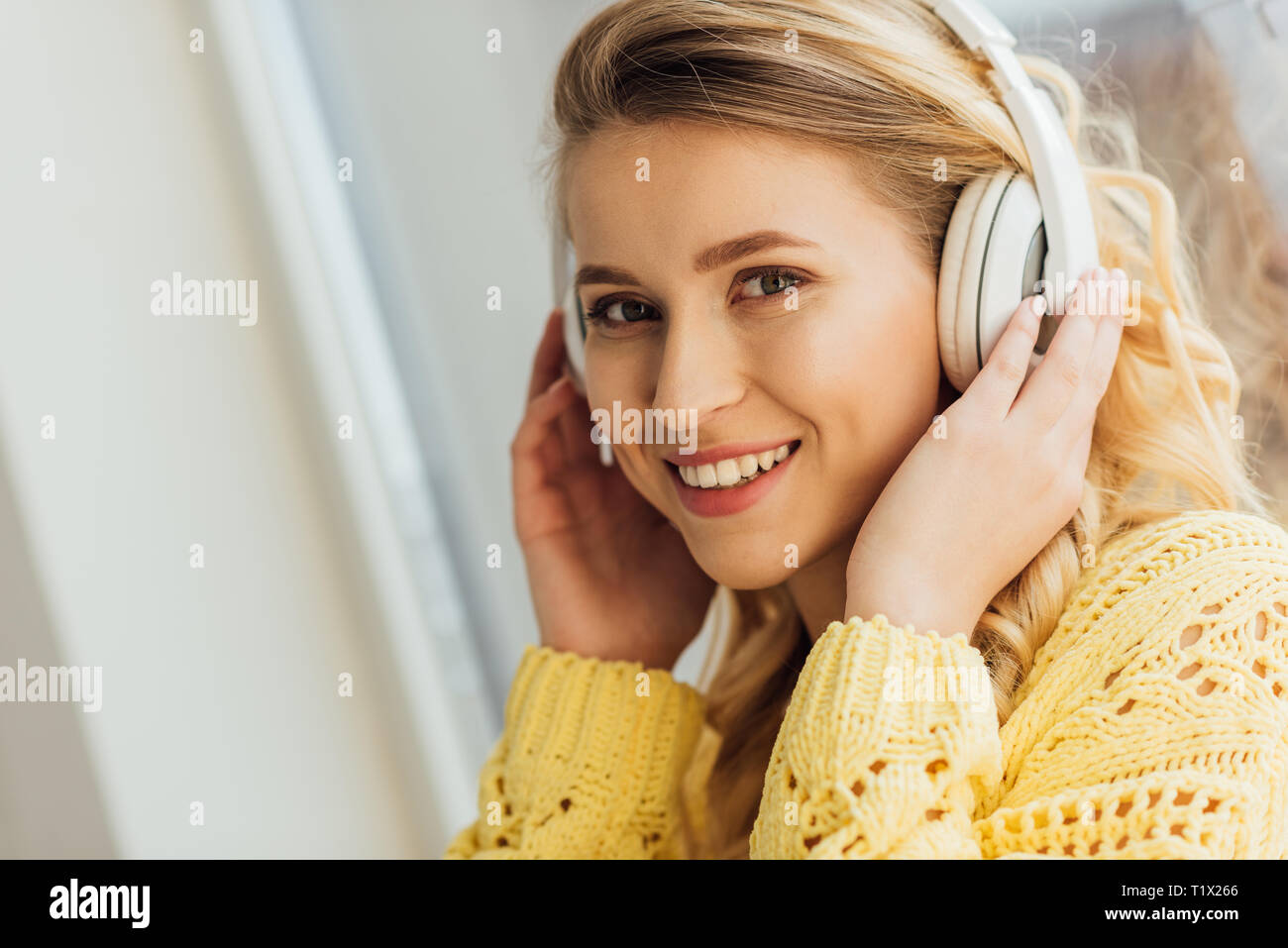 Beautiful smiling young woman in headphones looking at camera tout en écoutant la musique à la maison Banque D'Images