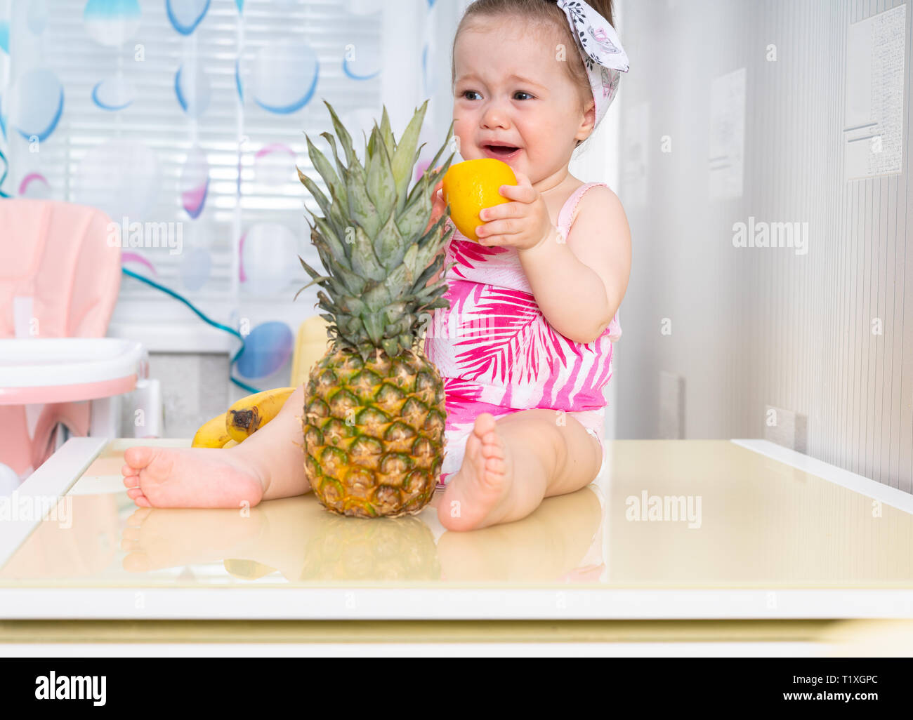 Jeune Fille Bebe Pleurer De Citron Aigre Assis Sur La Surface De La Table En Face D Un Ananas Photo Stock Alamy