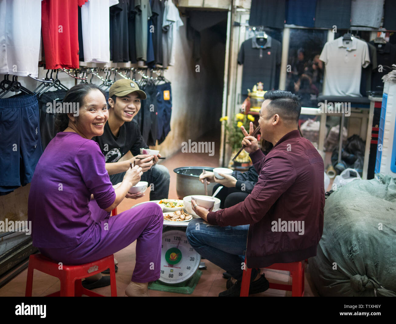 Les jeunes et le personnel de l'Vietmese heureux magasin de vêtements en train de dîner ensemble dans le magasin, Hanoi, Vietnam Banque D'Images