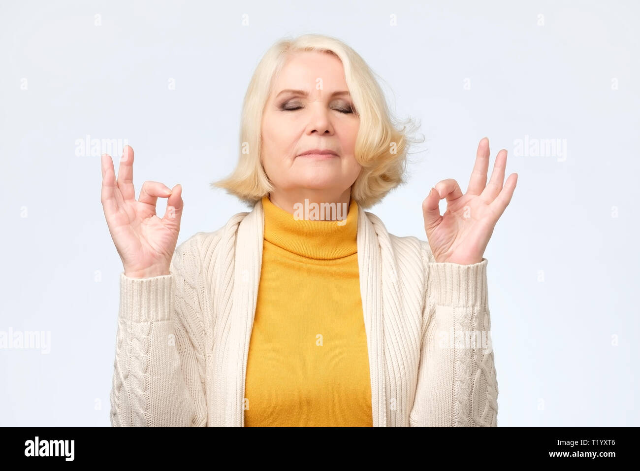 Senior woman smiling with eyes closed faisant le geste de la méditation avec les doigts. Concept de yoga. Banque D'Images