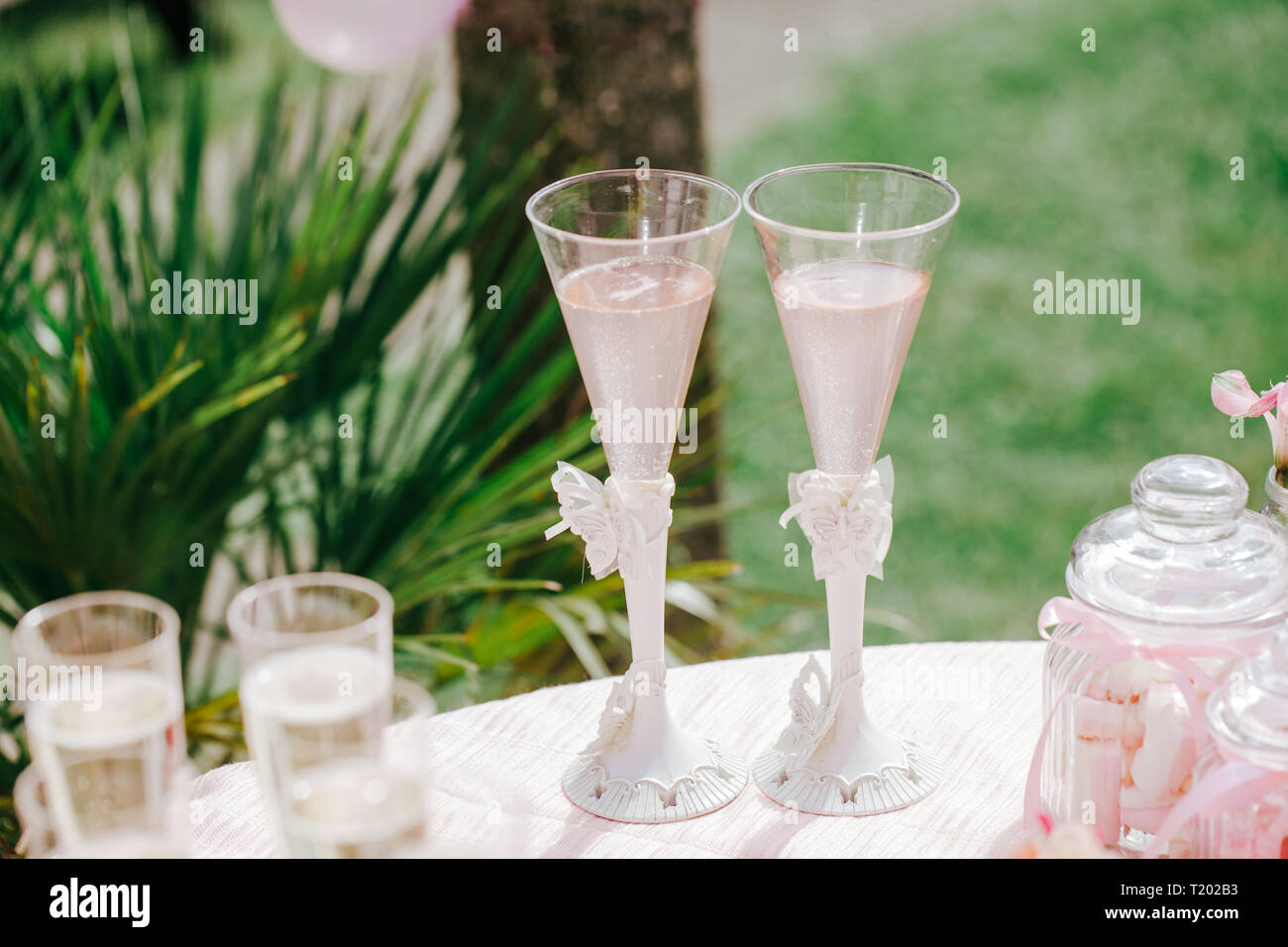 Deux verres de champagne rose sur la table, des bonbons dans le bocal, jardin outdoor party, fête, décor rose. Banque D'Images