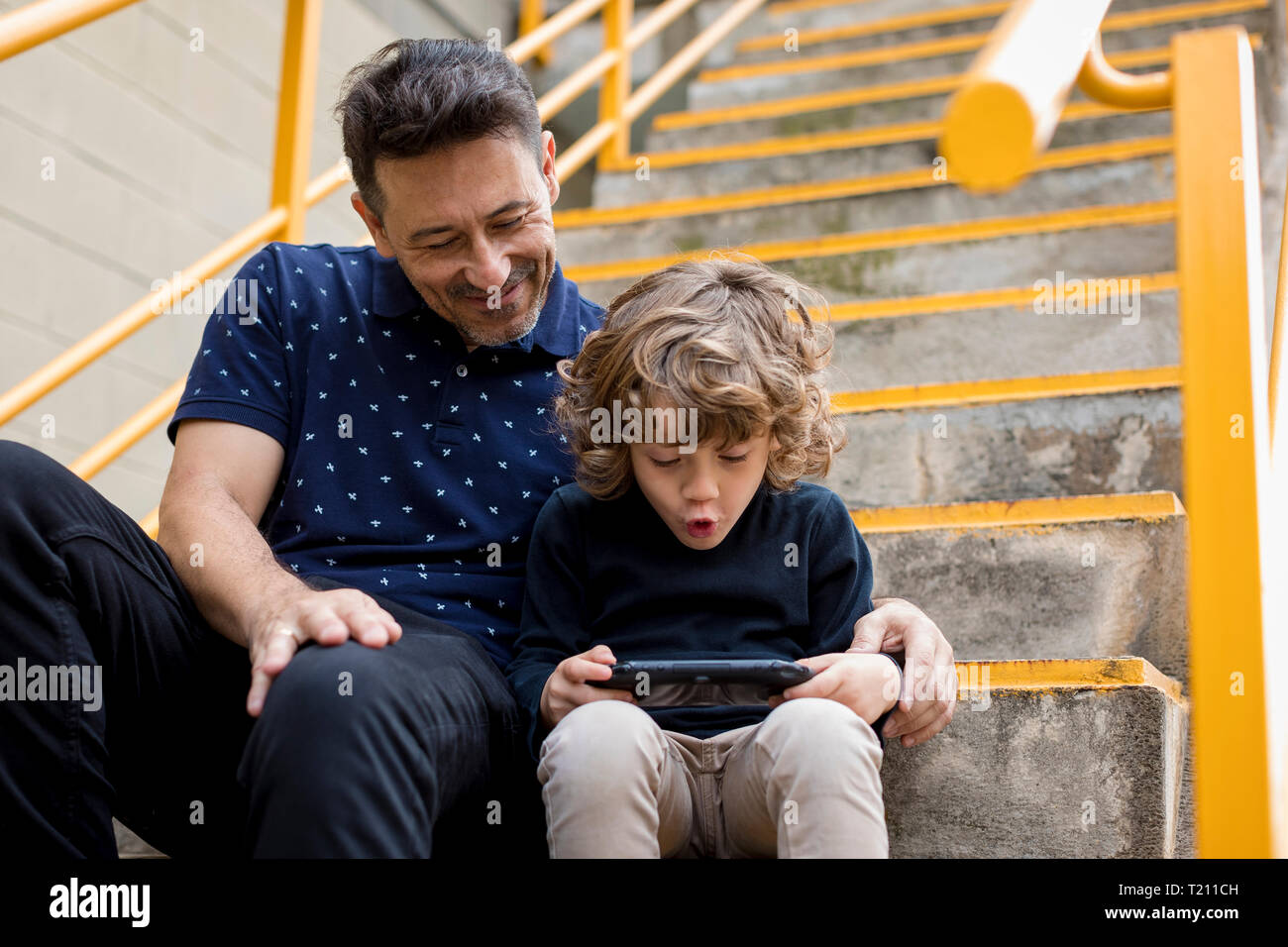 Père Fils regarder jouer avec la console de jeu de poche Banque D'Images