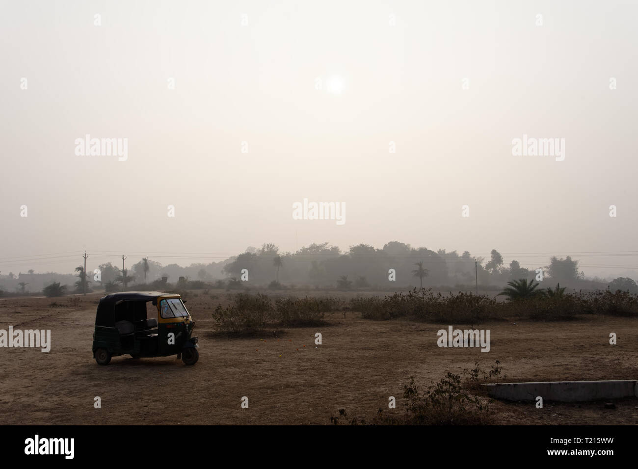 Auto-rickshaw indien se trouve isolé sur un vaste terrain sec au coucher du soleil. Banque D'Images