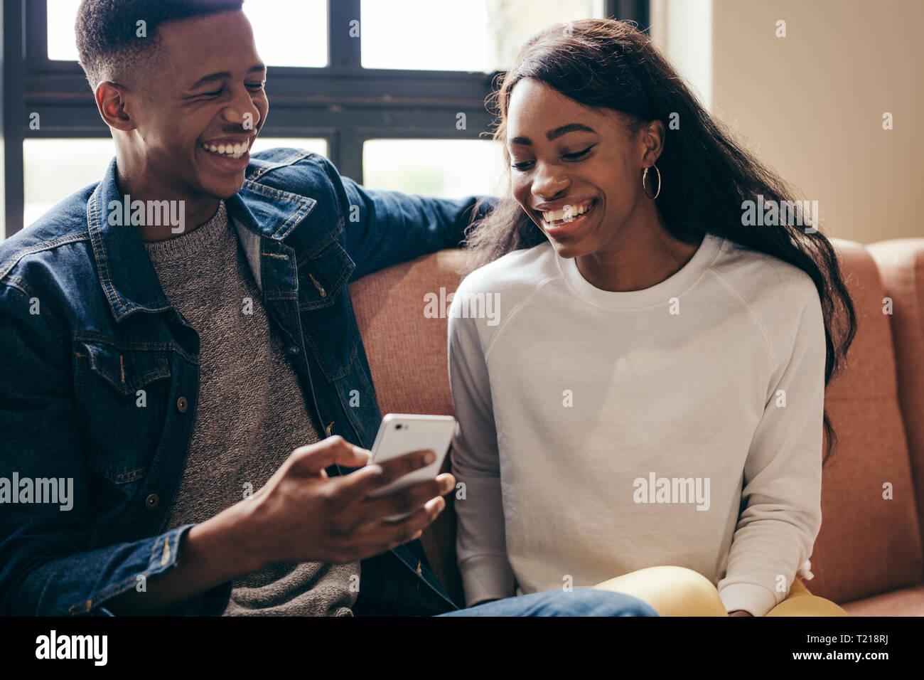 Deux étudiants américains africains using cell phone on campus. Heureux jeune homme et femme assise sur le canapé avec un téléphone intelligent. Banque D'Images