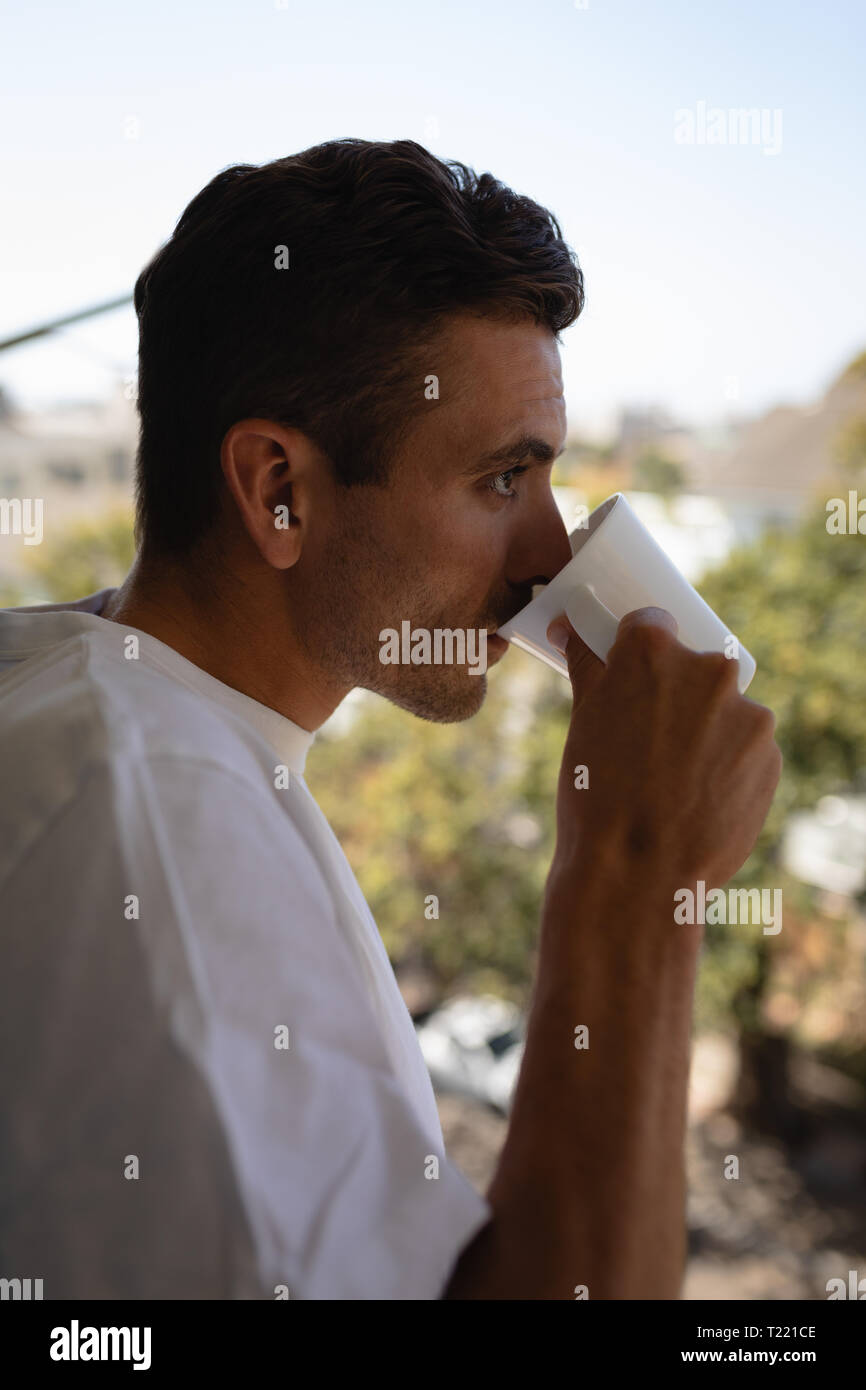 L'homme ayant une tasse de café tout en se tenant en balcon à la maison Banque D'Images
