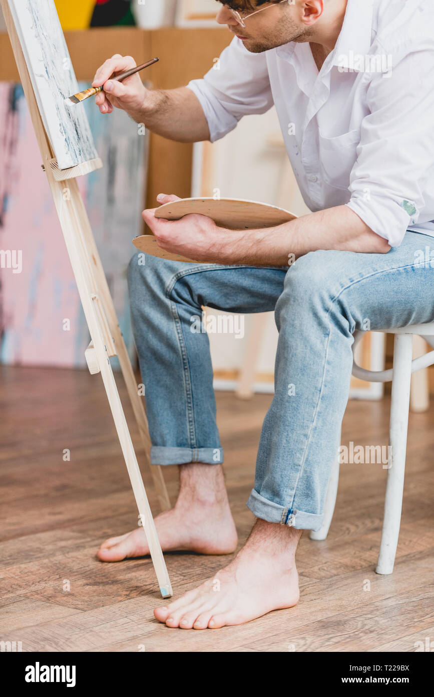 Vue partielle de l'artiste aux pieds nus en chemise blanche et un jean bleu  peinture sur toile Photo Stock - Alamy