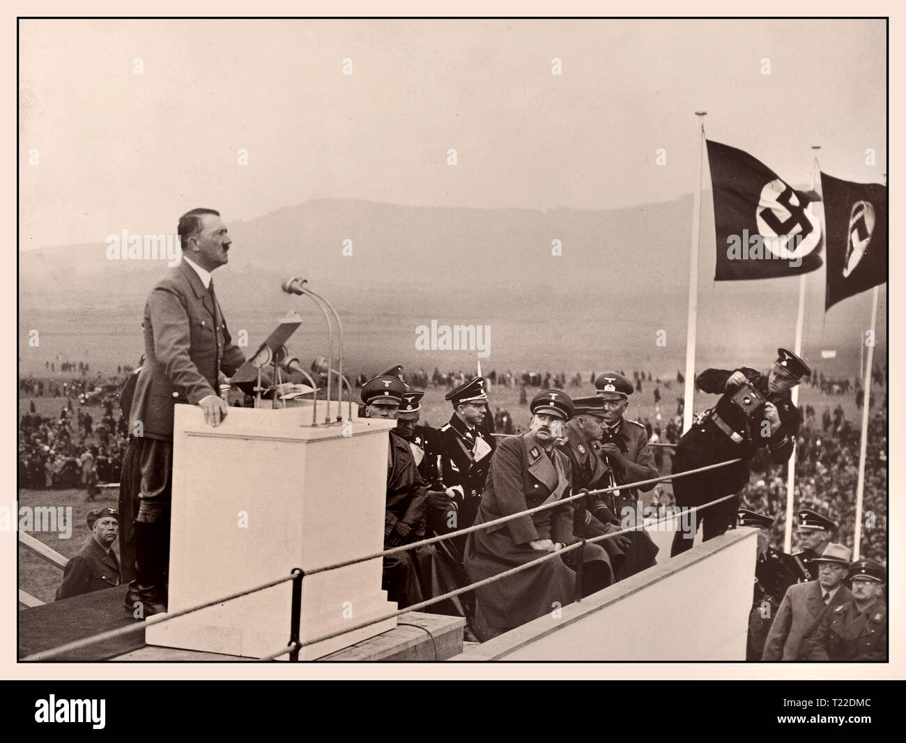 Vintage 1930 Droit d'Adolf Hitler avec des drapeaux à croix gammée, faisant un discours à partir d'un podium à l'extérieur - politique et homme d'état de l'Allemagne nazie, chancelier du Reich en 1933-1945, chef de l'Office national des travailleurs socialistes de l'Allemagne Banque D'Images