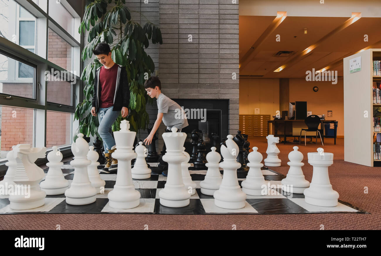 Deux jeunes garçons jouant le jeu d'échecs géant dans une bibliothèque Banque D'Images