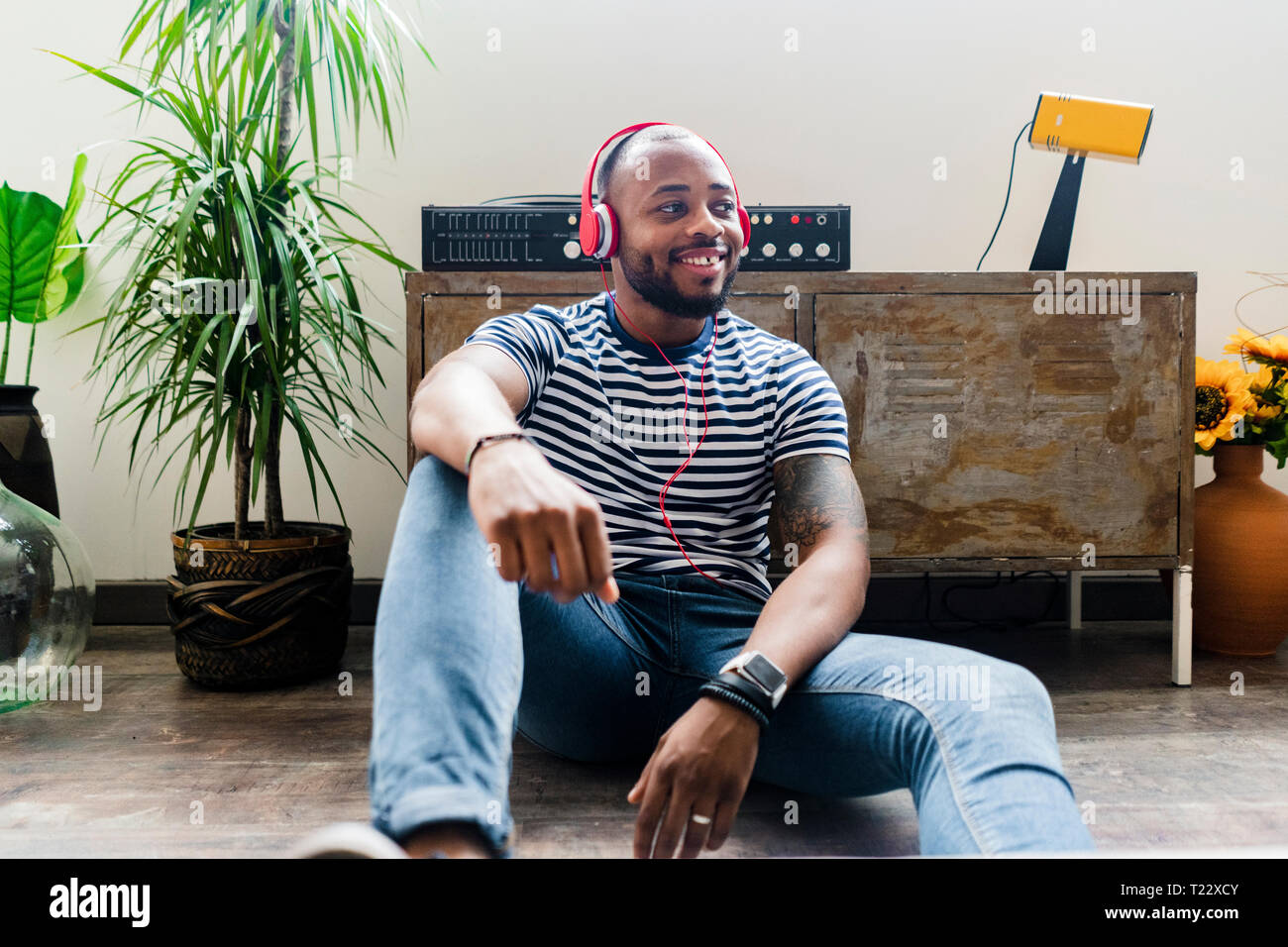 Smiling Young man with headphones sitting on floor dans un loft Banque D'Images