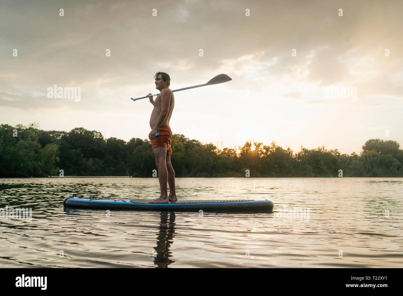 Homme debout sur le SUP sur un lac au coucher du soleil Banque D'Images